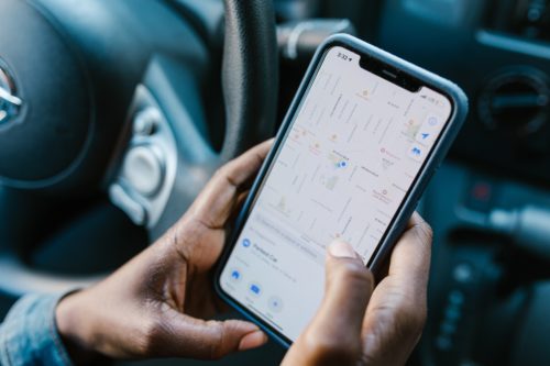 A person in a car is holding a smartphone displaying a map. The screen shows a GPS navigation app with streets and location pins, perfect for navigating Tampa. For those needing guidance after an Uber/Lyft accident, keeping contact info for the right lawyer is crucial.