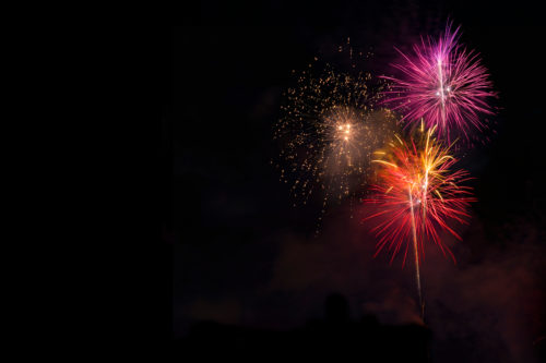 A colorful fireworks display lights up the night sky. Bursts of pink, orange, and gold create vibrant patterns on the dark background, casting reflections and sparkles—reminding us to enjoy safely and avoid any fireworks accidents.